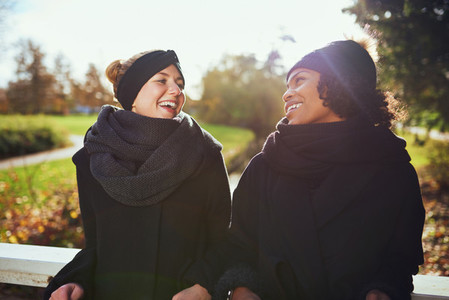 Two women in warm clothes standing on bridge in park