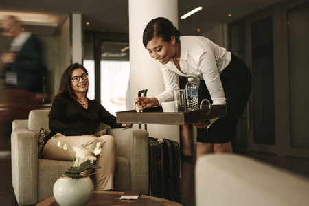 Airport lounge waitress serving coffee to female passenger
