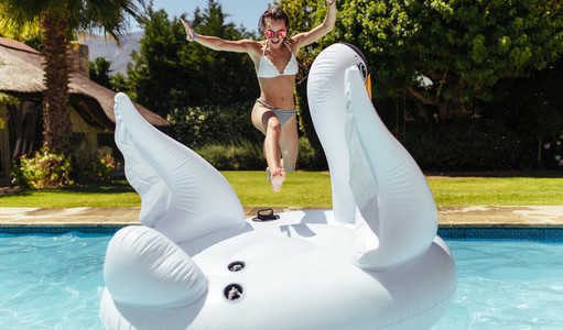 Woman jumping on to an inflatable toy in pool