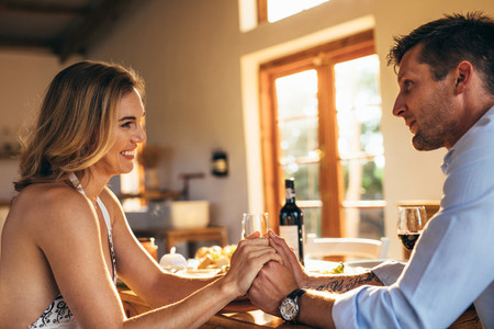 Loving young couple holding hands at dining table
