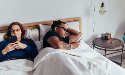 Young couple with smart phones in their bed