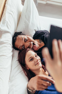 Crazy multiracial couple taking selfie on bed