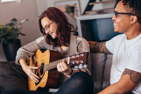 Woman playing guitar with her boyfriend at home