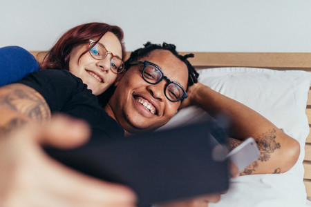 Multiracial couple taking selfie in bed
