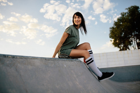 Female skateboarder sitting on a ramp in skate park