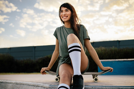 Attractive woman sitting on the skateboard at skate park