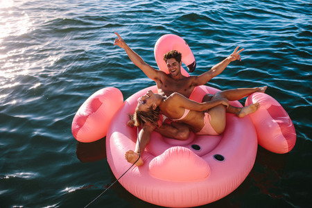 Excited couple riding on inflatable toy behind a boat
