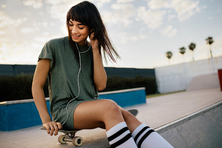 Beautiful girl listening music with earphones at skate park