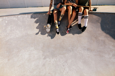 Legs of female skaters sitting together at skate park