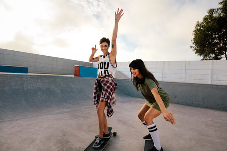 Female friends skateboarding together at skate park