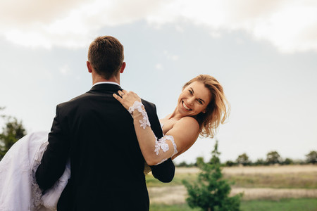 Groom carrying smiling bride on wedding day