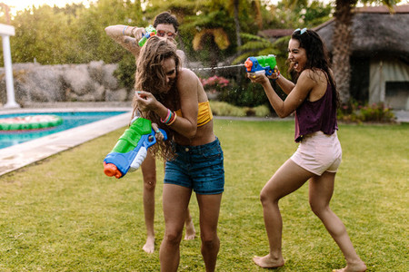 Happy friends doing water gun battle at poolside