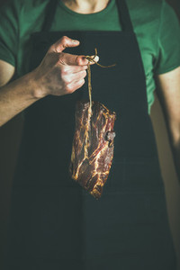 Man in black apron keeping cut of cured pork meat