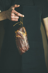 Man in black apron holding cut of cured pork