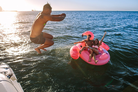 Man diving in sea with friends on inflatable toy