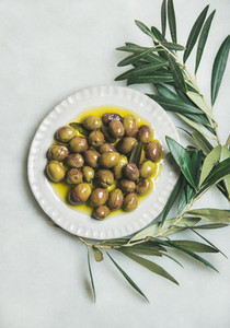 Pickled green olives and olive tree branch over marble background