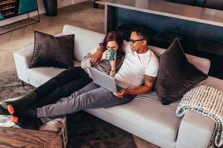 Interracial couple relaxing on sofa with laptop