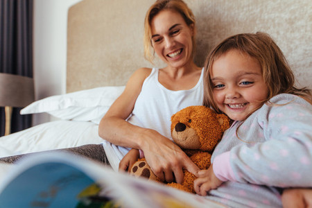Happy mother and daughter on bed reading book