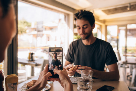 Woman capturing pictures of man eating burger