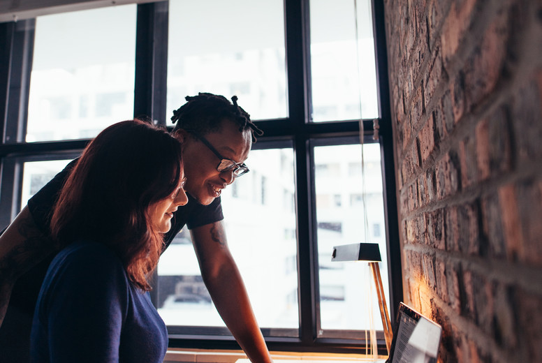 Woman working on laptop with man standing by