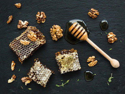Honeycomb  walnuts and honey dipper on black slate tray over grunge dark backdrop