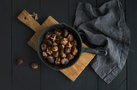 Roasted chestnuts in iron skillet pan on rustic wooden board