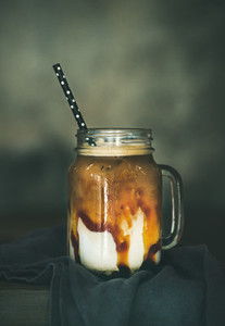Iced caramel macciato coffee with milk in jar on table
