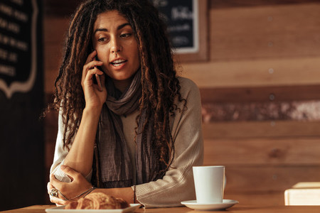 Woman talking over mobile phone at a cafe