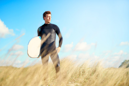 Surfer standing on a dune looking at the ocean
