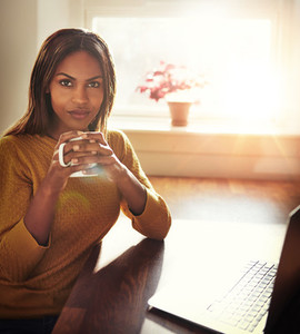 Woman holding coffee while seated near window