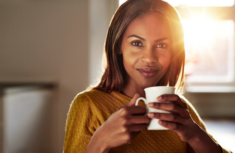 Smiling friendly young black woman drinking coffee