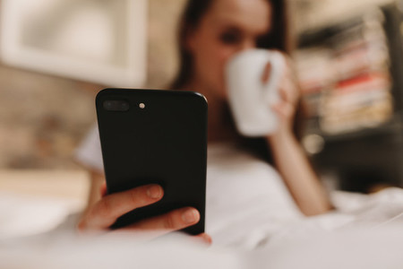 Woman drinking bed coffee looking at mobile phone