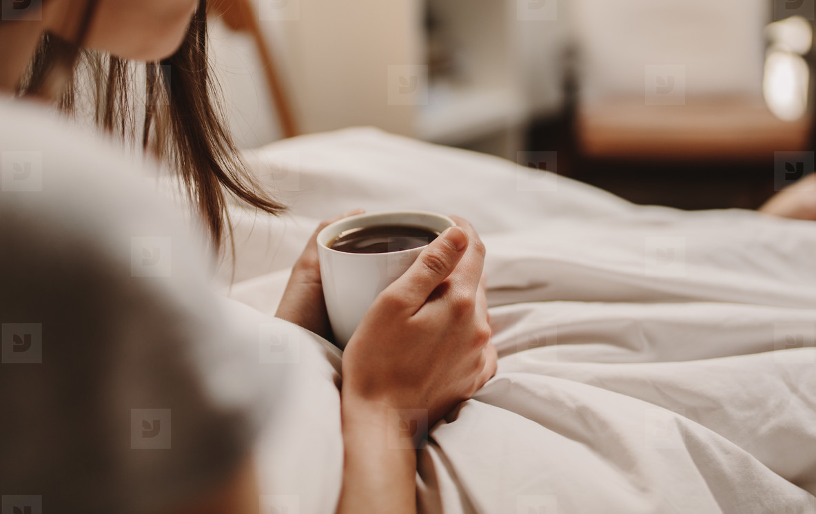 Woman holding a coffee cup sitting on bed (145935) - YouWorkForThem