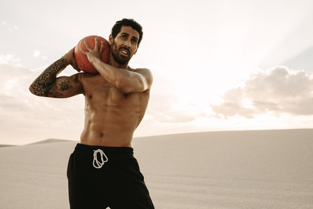 Athlete exercising with medicine ball on sand dunes