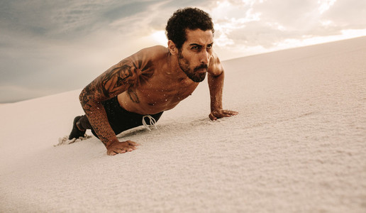 Fit man doing push ups over sand dune