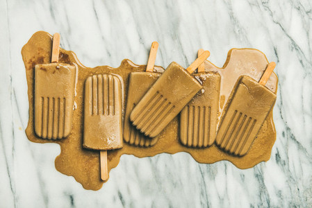 Flatlay of melting coffee latte popsicles on marble background