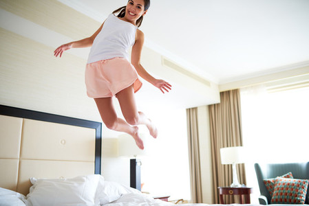 Angled view of woman jumping on bed
