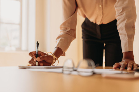 Businesswoman writing notes standing beside a table with hand re