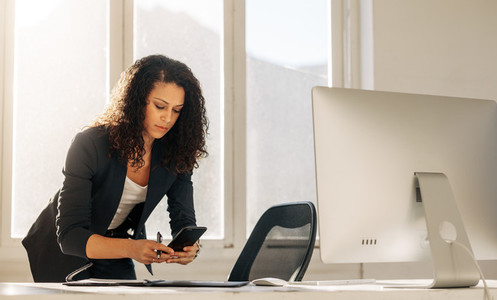 Woman entrepreneur using cell phone standing at her desk