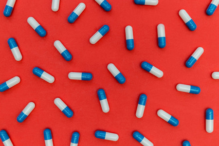 Drugs pills capsules on red background abstract concept
