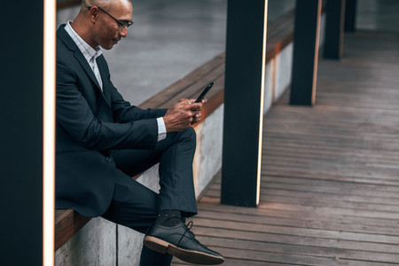 Businessman using mobile phone sitting outdoors