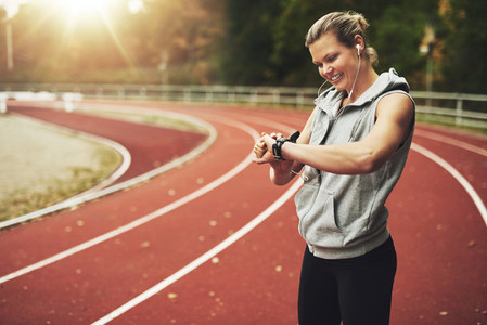 Young sportswoman looking at her watch while standing on track field