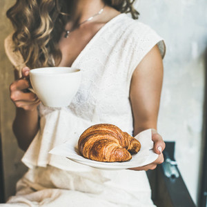 Blond woman holding croissant and cappuccino in cafe square crop