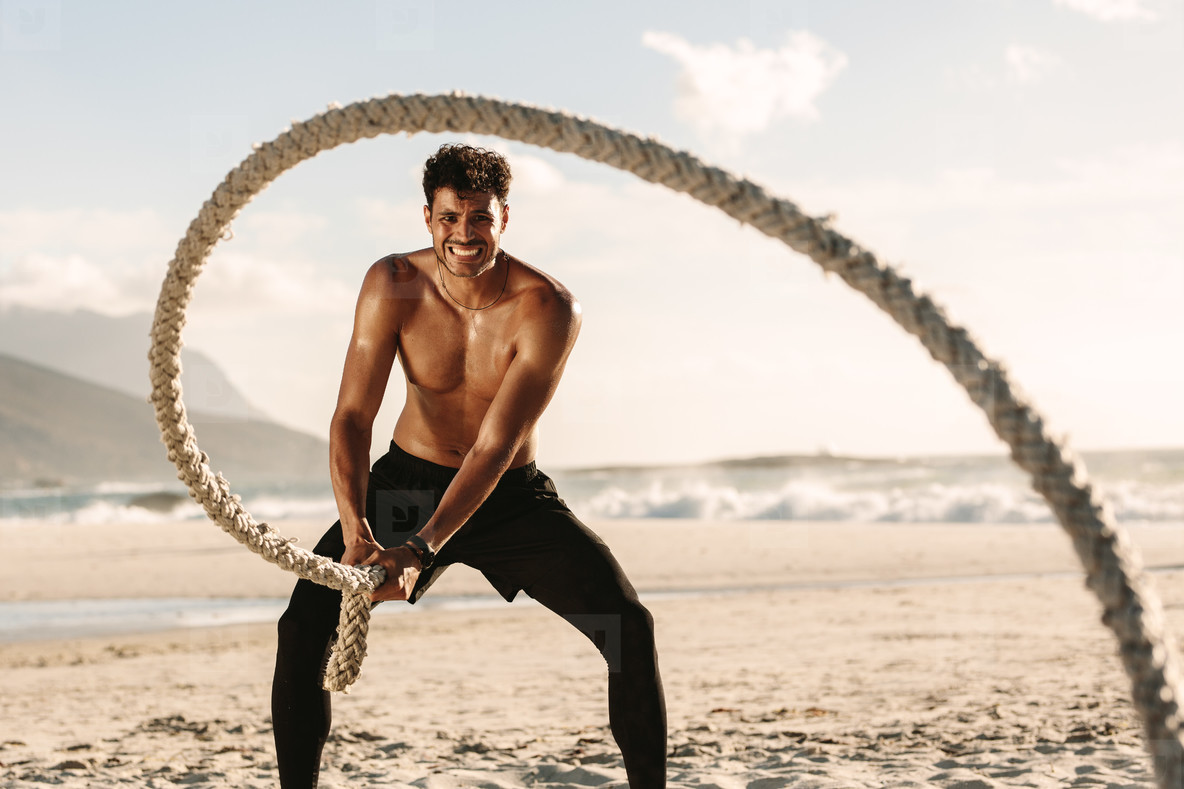 Man doing fitness training at the beach using battling rope