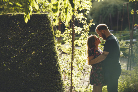 Young red headed couple embraced looking at each other in a urban garden with sun back light