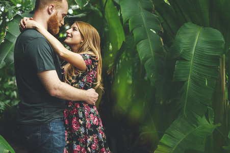 Young red headed couple embraced looking each other in a tropical grarden