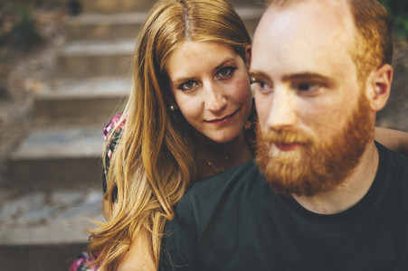 Young red headed woman looking at camera seated in stairs close to her boyfriend