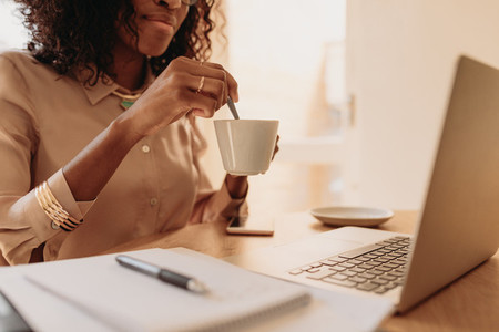 Woman holding a cup of coffee while working on laptop at home