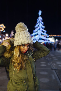 Portrait of a young woman at night with illuminated Christmas tree on background