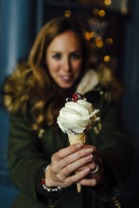 Young blonde woman showing ice cream at night with Christmas lights